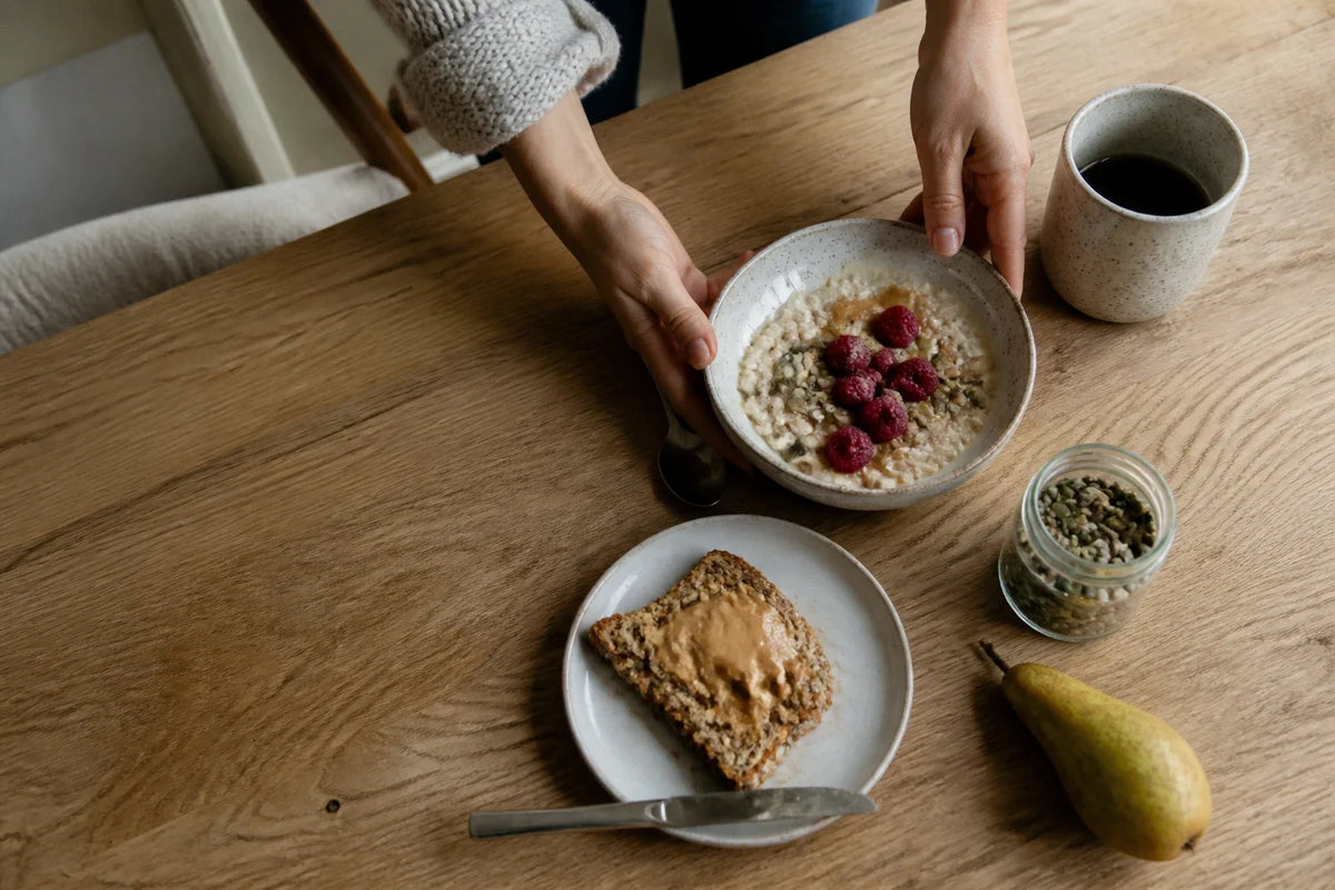 Porridge with raspberries and seeds beside seeded toast and a pear on a breakfast table