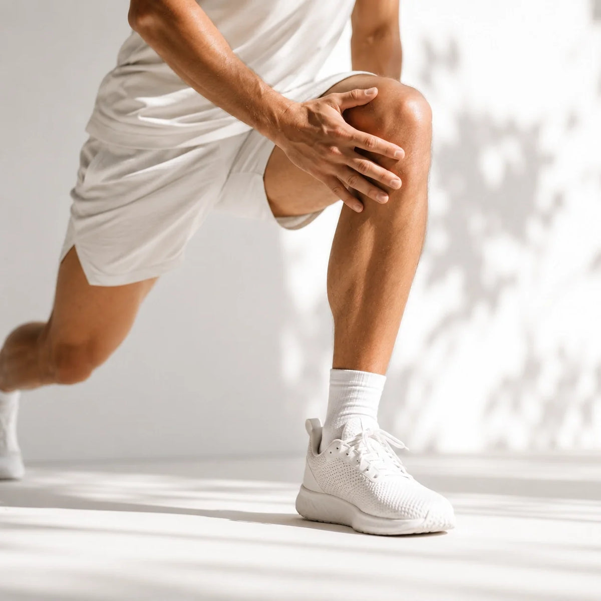 Active adult stretching knee in white sportswear in bright natural light