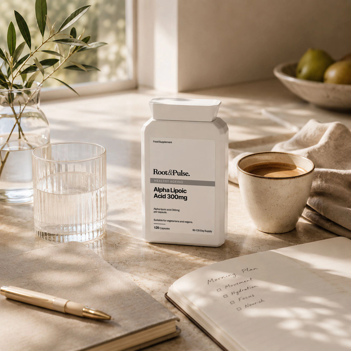 A white supplement bottle labeled Root & Pulse Alpha Lipoic Acid 300mg stands on a sunlit beige tabletop beside a glass of water, a cup of coffee, an open notebook, and a pen. The scene is styled with natural light, a vase with greenery, and fruit in the background.