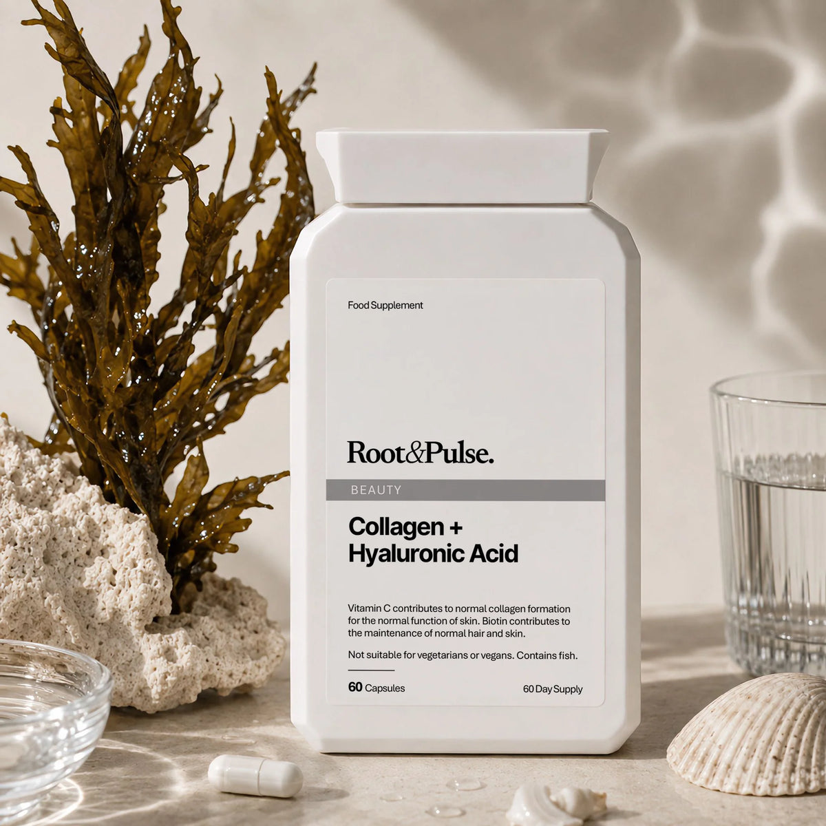 A white bottle of Root & Pulse Beauty Collagen + Hyaluronic Acid food supplement, styled on a stone surface with seashells, a glass of water, and dried seaweed.