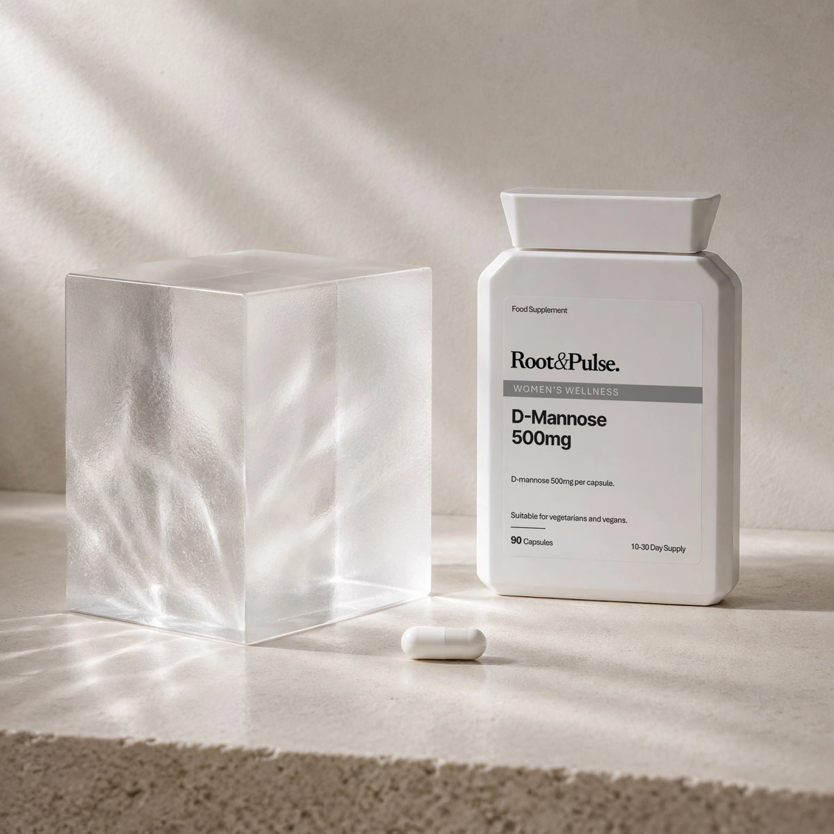 A white bottle of Root & Pulse D-Dmannose 500mg capsules stands on a light stone surface beside a translucent frosted cube and a single capsule, with soft diagonal shadows across the scene.
