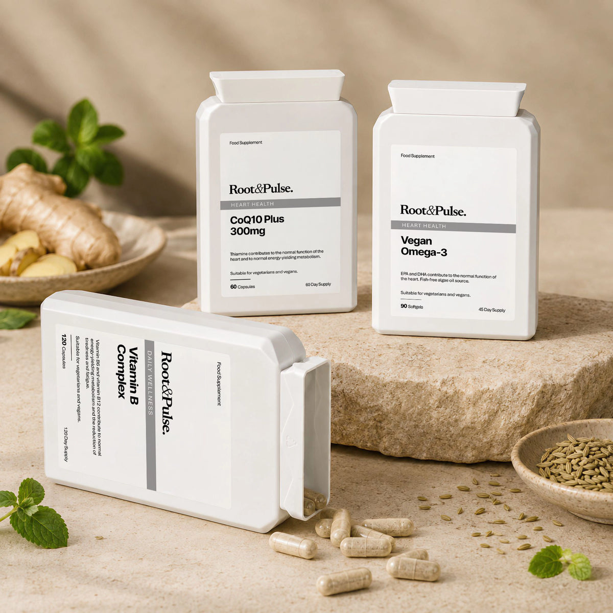 Three white supplement bottles from Root & Pulse are arranged on a beige stone surface with capsules scattered in front and small natural ingredients like ginger, mint, and seeds around them. The bottles include CoQ10 Plus 300mg, Vegan Omega-3, and Vitamin B Complex.