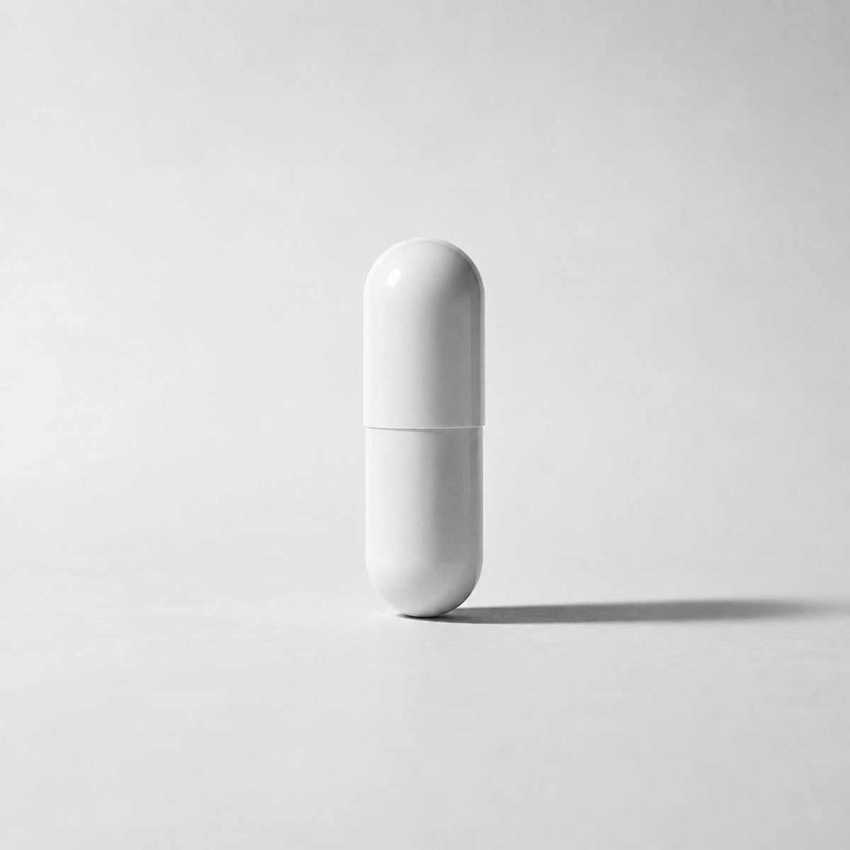 A minimalist white capsule-shaped container standing upright on a light gray surface against a matching gray background.
