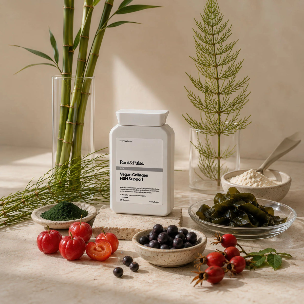 A white bottle of Root and Pulse Vegan Collagen HSN Support supplement stands on a stone surface surrounded by natural ingredients including tomatoes, blueberries, kelp, green powder, and bamboo in glass vases.