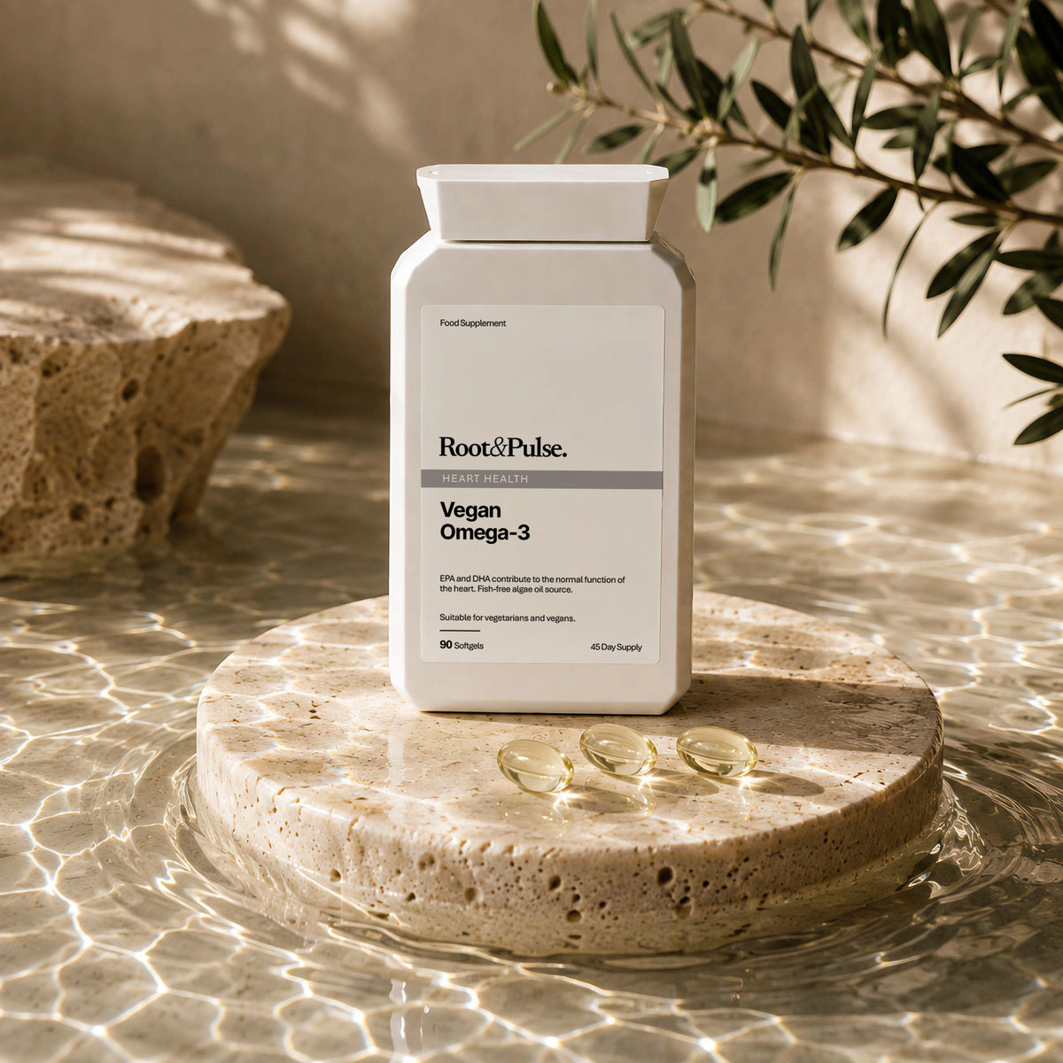 A white bottle of Root & Pulse Vegan Omega-3 dietary supplement stands on a round stone pedestal in shallow water, with three softgel capsules placed in front and olive branches overhead.
