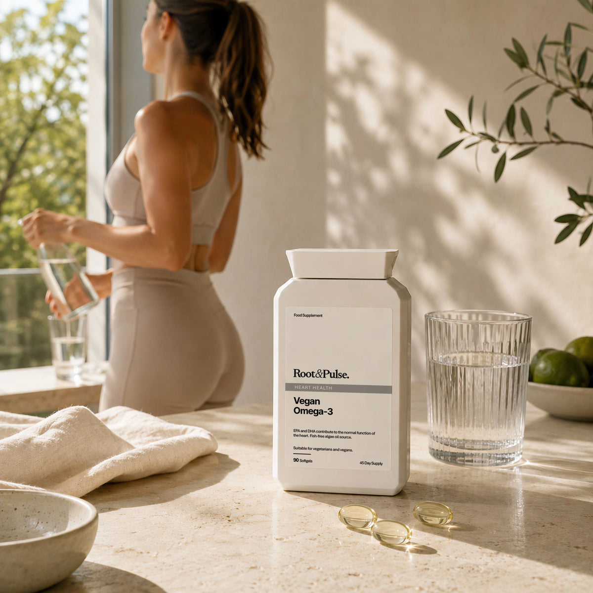 A bottle of Root&Pulse Vegan Omega-3 dietary supplement sits on a marble countertop next to a glass of water and a few softgel capsules, with a woman in athletic wear standing in the background near a window.