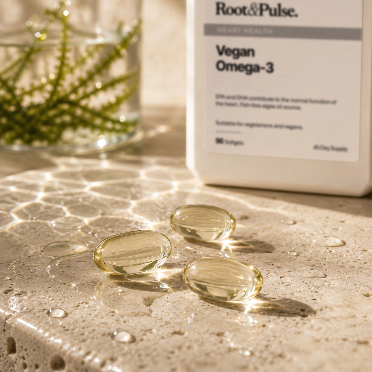 Three clear softgel capsules filled with golden-yellow liquid sit on a sunlit stone surface with water droplets, next to a white Root & Pulse Vegan Omega-3 bottle.
