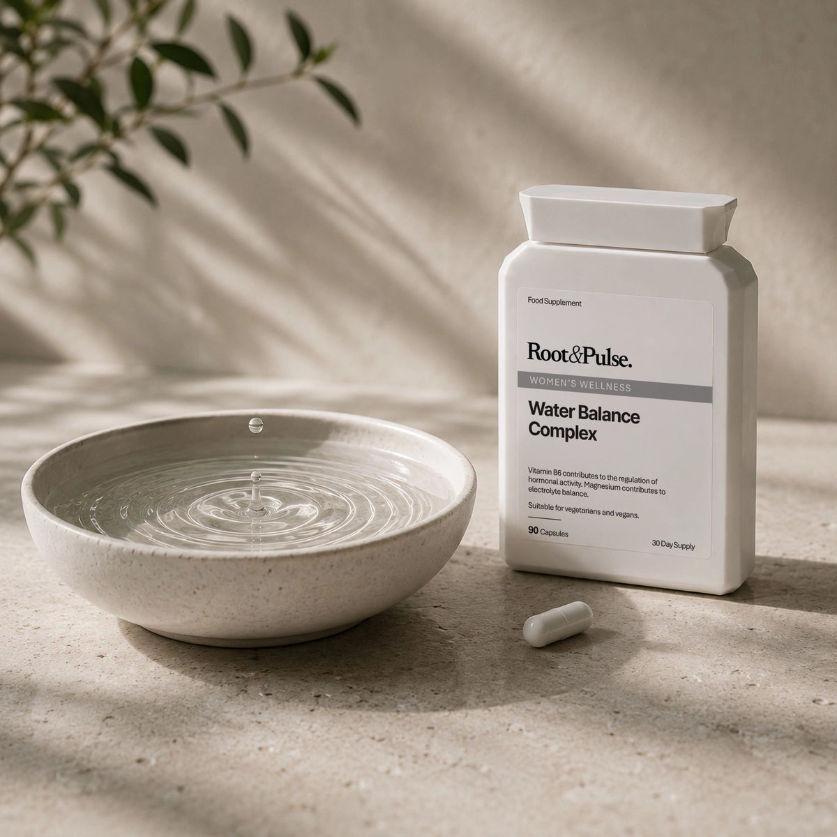 A white bottle of Root of Pulse Water Balance Complex dietary supplement stands next to a ceramic water bowl with ripples and a single capsule on a textured stone surface.