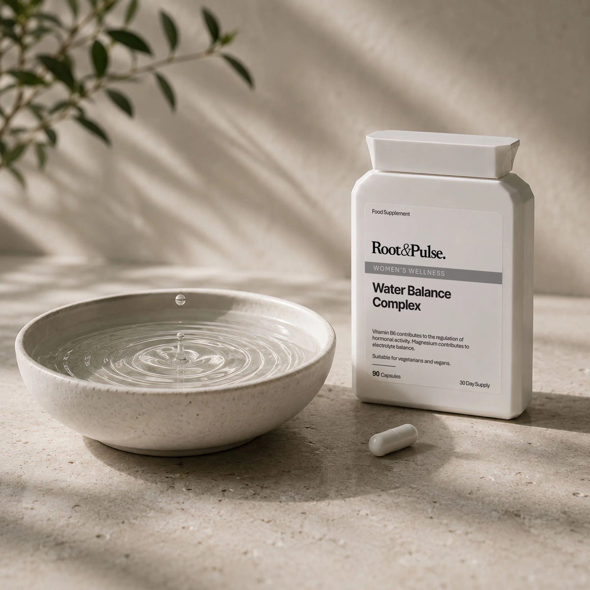 A white bottle of Root of Pulse Water Balance Complex dietary supplement stands next to a ceramic water bowl with ripples and a single capsule on a textured stone surface.