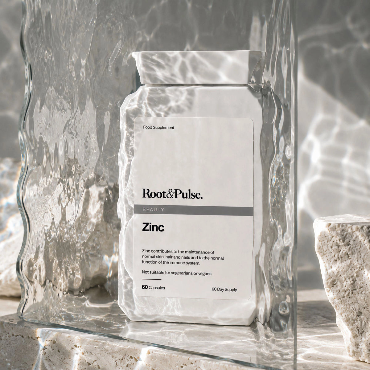 A white bag of Root & Pulse Beauty Zinc dietary supplement capsules, styled inside a clear glass vessel with water ripples and light reflections.